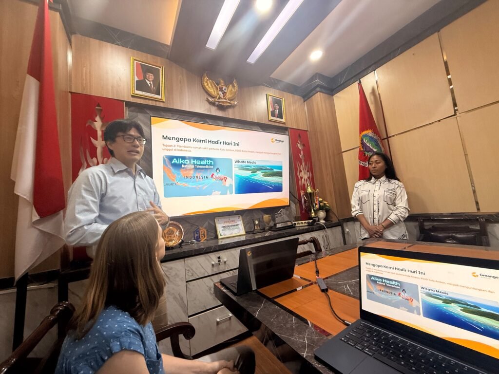 A Gmango presentation on Aiko Health in a wood-paneled meeting room with Indonesian flags