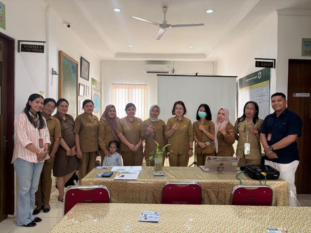 Staff and visitors pose in a meeting room at Puskesmas Karpan, with a laptop on the table